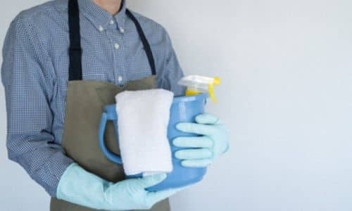 foto di un addetto alla pulizia con camice, guanti e in mano i prodotti chimici per pulire